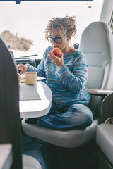 View of young woman sitting and having leisure time inside a camper van motor home. Healthy...