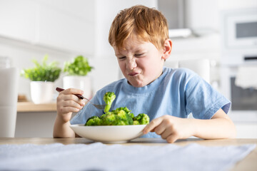 The little boy looks with distaste at the broccoli on his fork