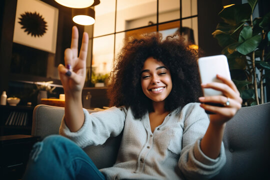 Happy afro American woman relaxing on the sofa at home. Girl taking selfie picture with smartphone