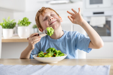A cute little boy is eating broccoli for lunch and he likes it very much