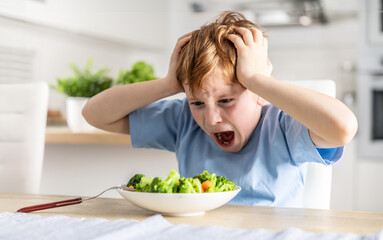 Shocked and upset little boy because he has to eat broccoli for dinner, which he doesn't like