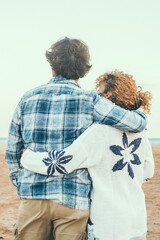 Rear view portrait of couple in love admiring the beach and ocean hugging with love. Romantic life...
