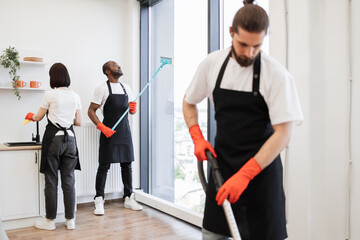 Focus on positive African American worker cleaning panoramic window glass with mop in modern...