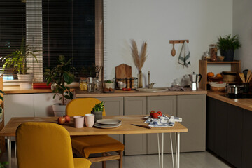 Yellow chairs on both sides of wooden table with kitchenware, green domestic plant in striped flowerpot, towel and fresh apples