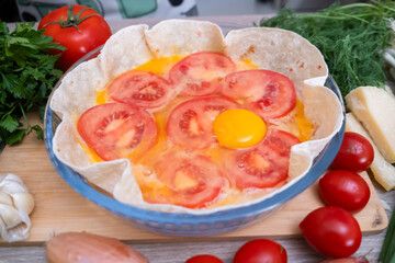 Uncooked tortilla with egg and tomatoes prepared for baking on wooden cutting board background