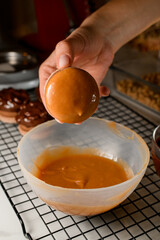 Female confectioner's hand holds a macaroon dipped in caramel-colored cream