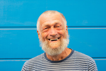 75 year old senior man laughs while having a good time outdoors. Portrait with blue background....