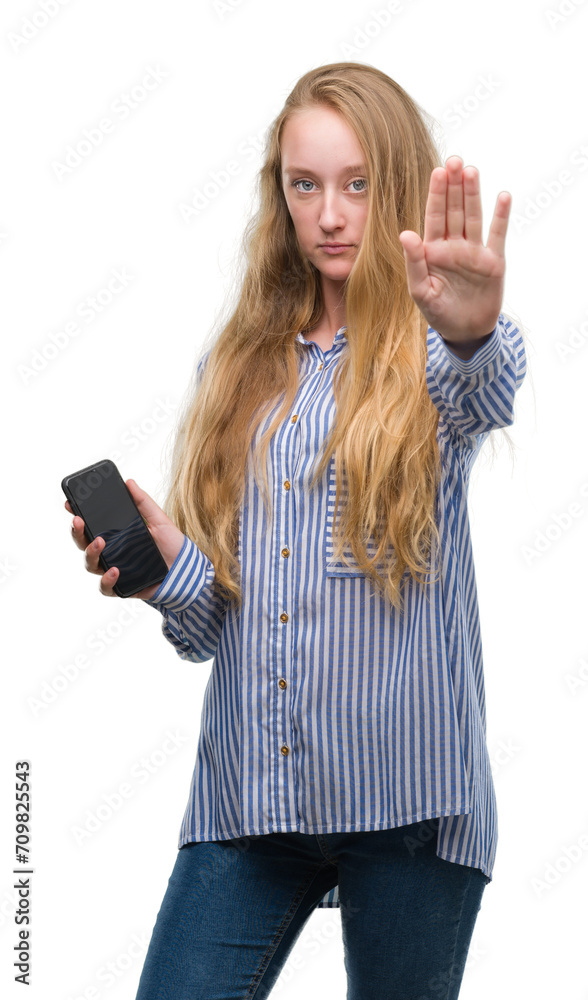 Sticker Blonde teenager woman using smartphone with open hand doing stop sign with serious and confident expression, defense gesture