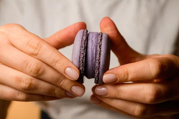 Rolgordijnen Close-up female hands of a confectioner fasten the halves of purple macaroons © fesenko