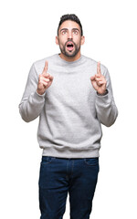 Young handsome man wearing sweatshirt over isolated background amazed and surprised looking up and pointing with fingers and raised arms.