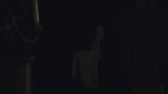 A young woman in a white long dress sits on a chair in a dark Gothic church. Bright sun rays and contrasting shadows. Prayer. Meditation and expression. Fashion and Cinematic concept