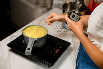 Woman confectioner controls the preparation of syrup with a kitchen thermometer