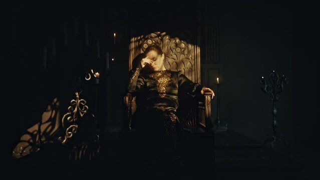 A young woman in a black long dress sits in a wooden carved throne in a dark Gothic church. Meditation and expression. Fashion and Cinematic concept
