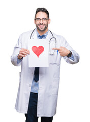 Handsome young doctor man holding paper with red heart over isolated background very happy pointing with hand and finger