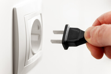 Hand connects an american electric plug into a white european socket or white wall outlet