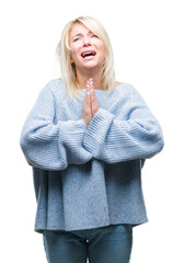 Young beautiful blonde woman wearing winter sweater over isolated background begging and praying...