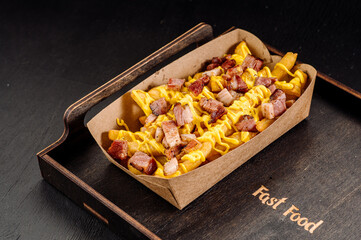 Delicious fast food French fries with bacon and cheese sauce in a take-out cardboard box