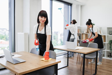 Portrait of Caucasian young woman holding sponge, detergent cleaning on table in office room...