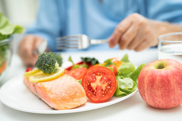 Asian elderly woman patient eating salmon steak breakfast with vegetable healthy food in hospital.