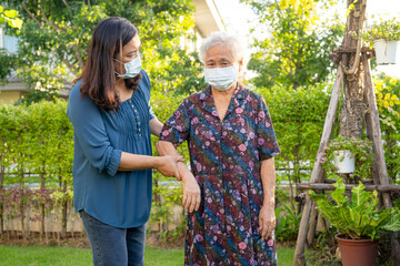 Caregiver help Asian elderly woman patient wearing face mask walk in park, healthy strong medical concept.