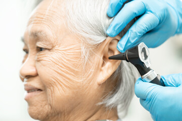 Audiologist or ENT doctor use otoscope checking ear of asian senior woman patient treating hearing loss problem. - obrazy, fototapety, plakaty