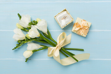 White freesia flower and gift box with diamond ring on wooden background, top view