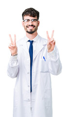 Young professional scientist man wearing white coat over isolated background smiling looking to the camera showing fingers doing victory sign. Number two.