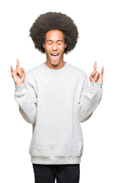 Young african american man with afro hair wearing sporty sweatshirt shouting with crazy expression doing rock symbol with hands up. Music star. Heavy concept.