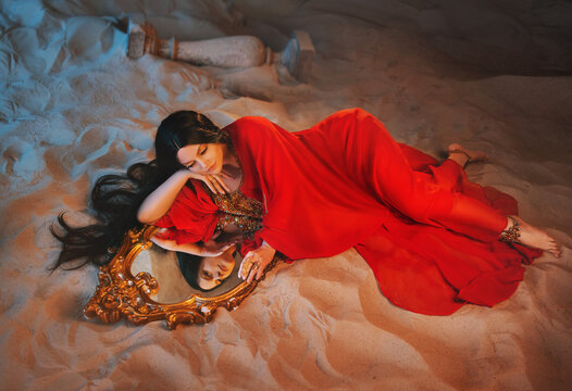 art Portrait real Fantasy girl arabic woman Fairy queen looks at reflection in mirror magic. beauty girl Lies in room full sand desert. red long dress dream face fairy style night moon light uae dubai