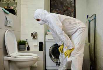 Young man in protective workwear bending over ceramic toilet bowl after flushing while cleaning it...