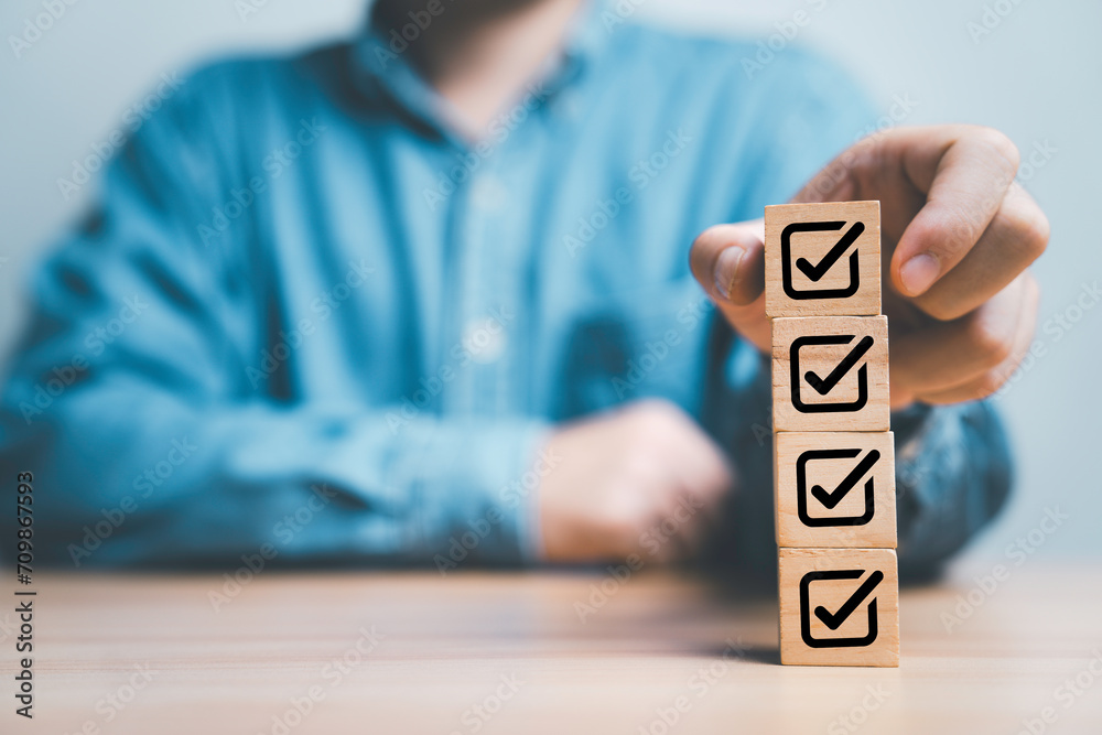 Poster Businessman stacking correct tick sign mark on wooden block cube for approve quality assurance  guarantee and continuous improvement concept.