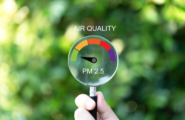 Hand holding magnifier glass with good air quality indicator scale on greenery background which...
