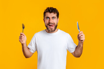 Hungry young guy holding knife and fork on yellow background