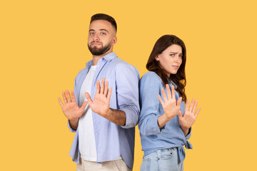 Couple gesturing stop with hands, standoffish poses, yellow background