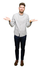 Young handsome man wearing casual shirt clueless and confused expression with arms and hands raised. Doubt concept.