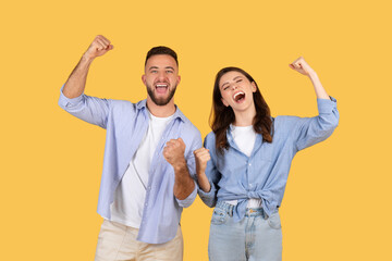 Joyful european couple cheering with raised fists, yellow background