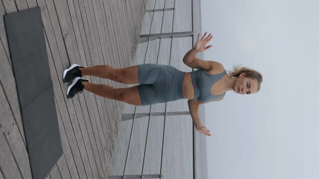 Vertical shot of Determined and focused, an athletic young woman in sportswear trains outdoors, performing jumping jacks on a bridge for an effective and energetic fitness routine