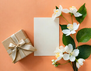 Greeting, invitation blank card with white jasmine flowers and gift box on trendy peach color background, copy space. Mock up. Flat lay. Top view. Romantic wedding holiday celebration concept