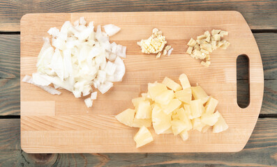 Chopped spices garlic, onions with ginger and pineapple pieces on a cutting board.