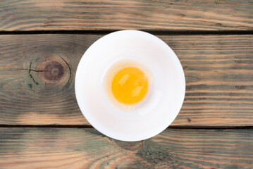 Raw chicken egg yolk is separated with white in a white bowl.