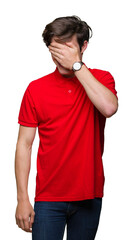 Young handsome man wearing red t-shirt over isolated background smiling and laughing with hand on face covering eyes for surprise. Blind concept.