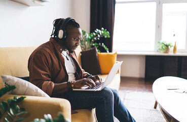 Black man with headphones working on laptop in living room
