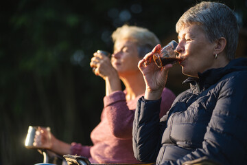 Naklejka premium Smart Elderly female friends or retired couple are laughing and enjoying cup of coffee and chatting in the early morning while on vacation, journey trip. Quality time of senior adult outdoor activity.