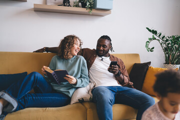 Cheerful multiethnic couple sitting on sofa while spending time together