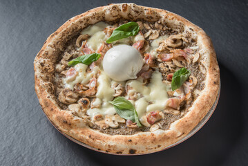 Italian pizza with mozzarella , bacon , mushrooms and truffle sauce isolated on black stone table 
