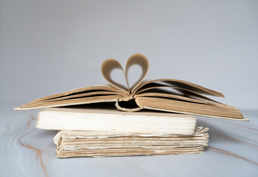 Pile de livres anciens avec un livre ouvert sur le dessus et des pages qui forment un coeur