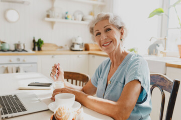 Side view of happy cute charming charismatic caucasian grandma with gray hair having breakfast in...