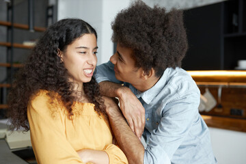 Pretty african american girl with folded arms showing teeth to her boyfriend with afro hair asking...