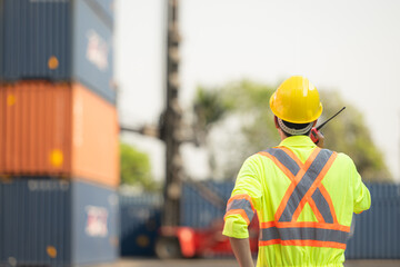 Workers in the import and export industry use walkie talkies to communicate with drivers of reach stacker containers in an empty container warehouse.
