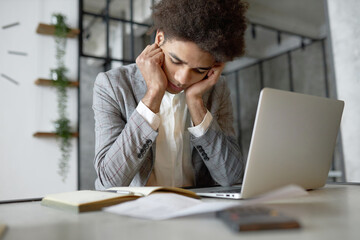 Fototapeta premium Selective focus on young upset tired exhausted puzzled african american man developer in plaid suit sitting in front of laptop, working in office, reading manual, having troubles launching new project